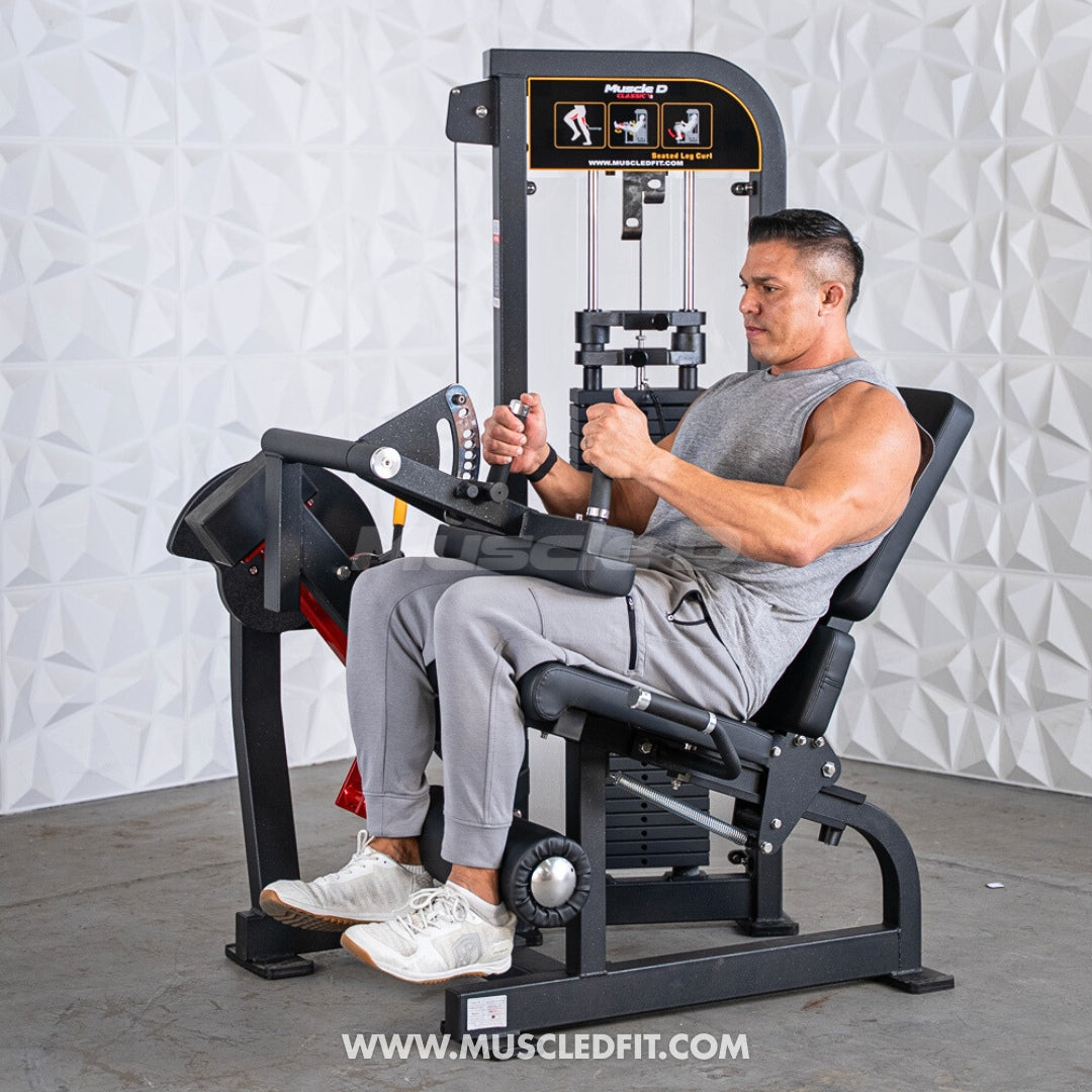 Man using a Classic V2 Seated Leg Curl machine in a gym setting with a textured white wall background.