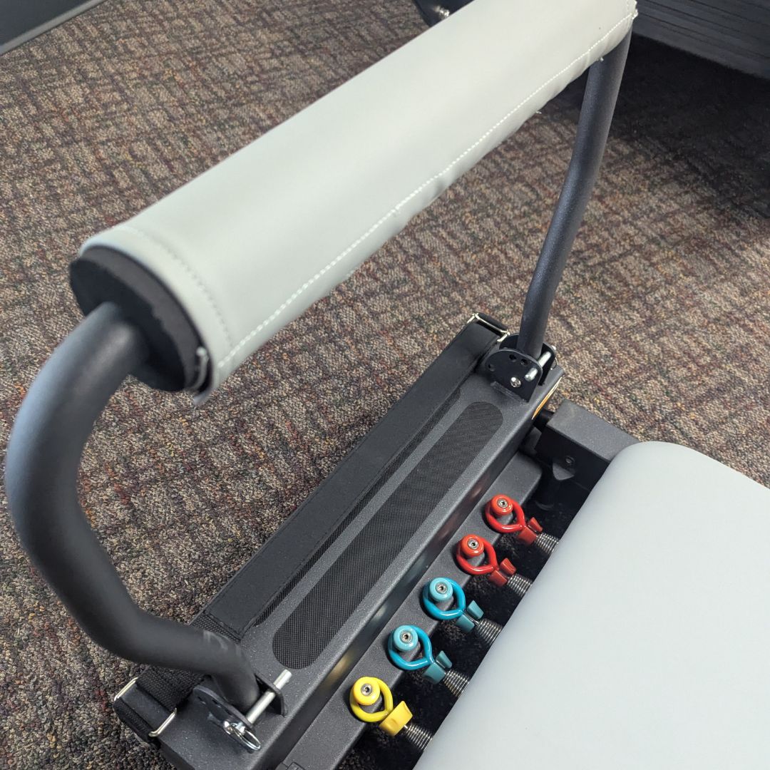 sleek light grey pilates reformer table with padded platform, adjustable foot bar, and sturdy metal frame for home or studio use