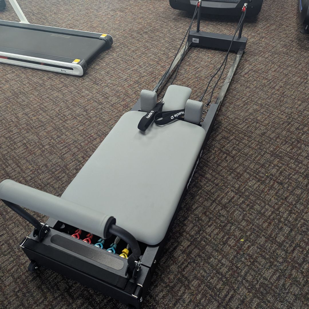 sleek light grey pilates reformer table with padded platform, adjustable foot bar, and sturdy metal frame for home or studio use