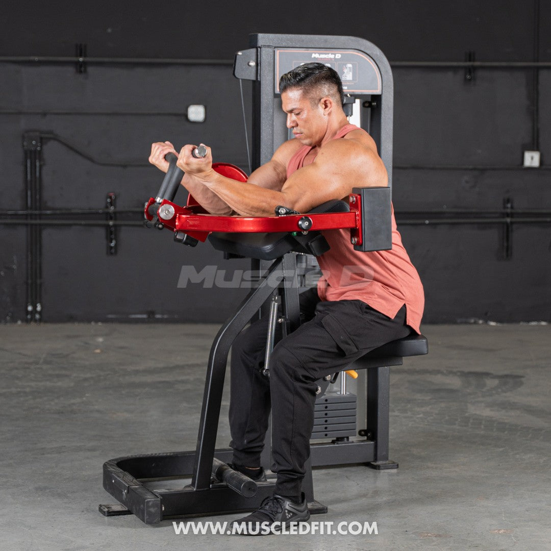 Man exercising on a red and black Classic V2 Biceps Curl machine with 'Muscle Fit' branding.
