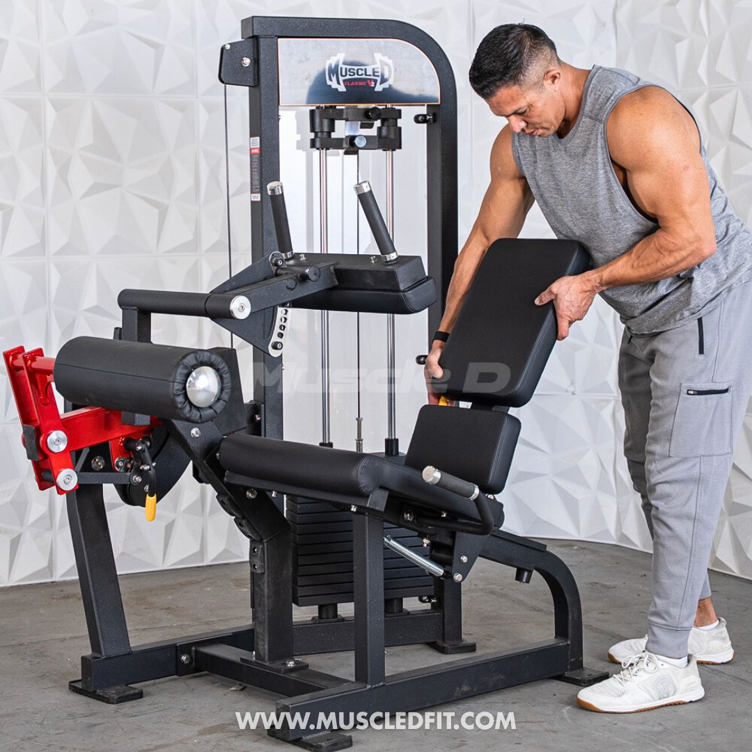 Man adjusting a Classic V2 Selectorized Leg Extension / Seated Leg Curl Combo machine with 'Muscle Fit' branding in the background.