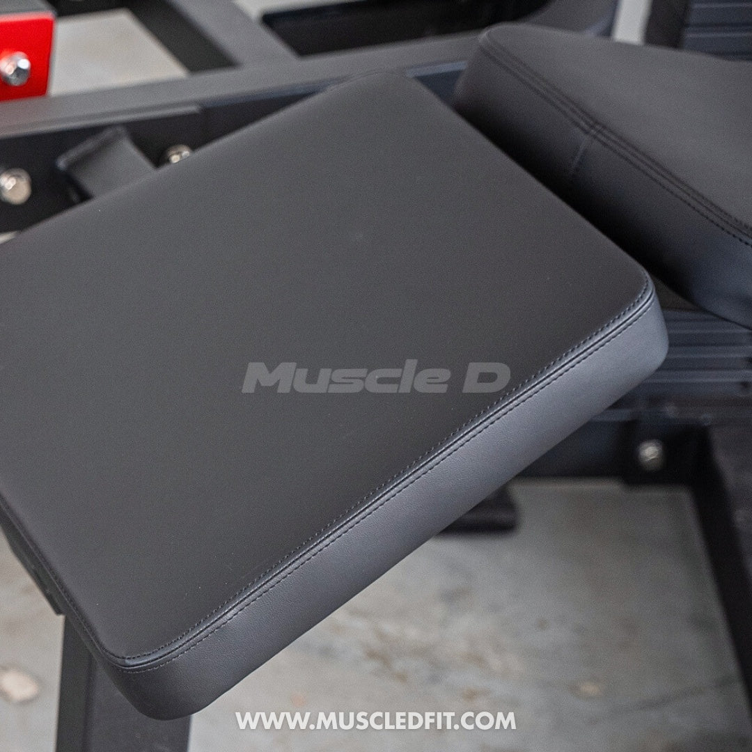  Close up of the Classic V2 Prone Leg Curl Pad with 'Muscle D' branding on a blurred background