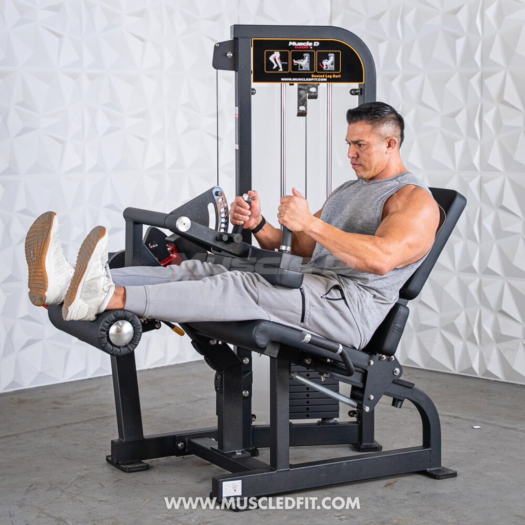 Man using a Classic V2 Seated Leg Curl machine in a gym setting with a textured wall background.
