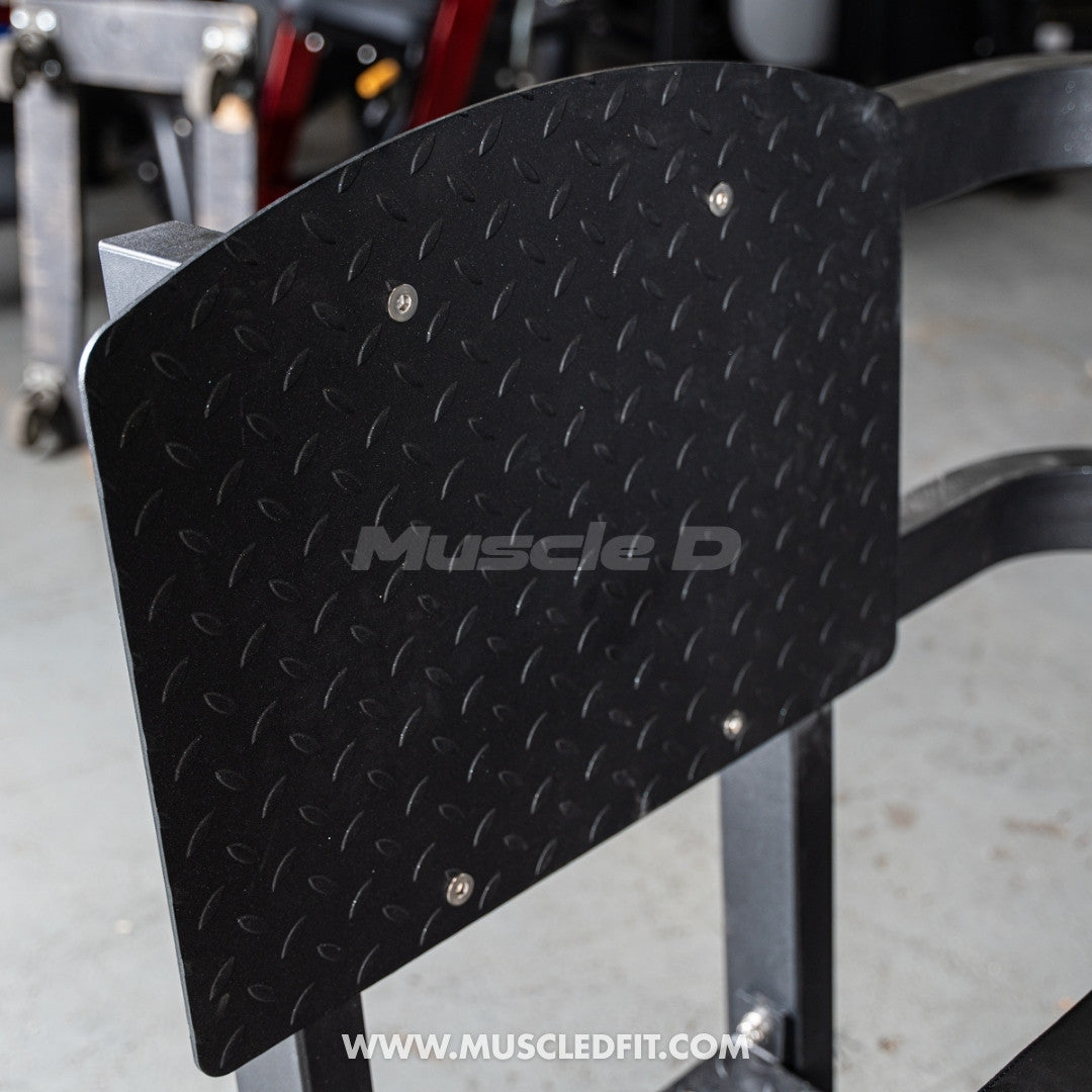 Black metal foot plate with diamond plate pattern  for Classic V2 Selectorized Leg Press with'Muscle D' branding on a blurred background.
