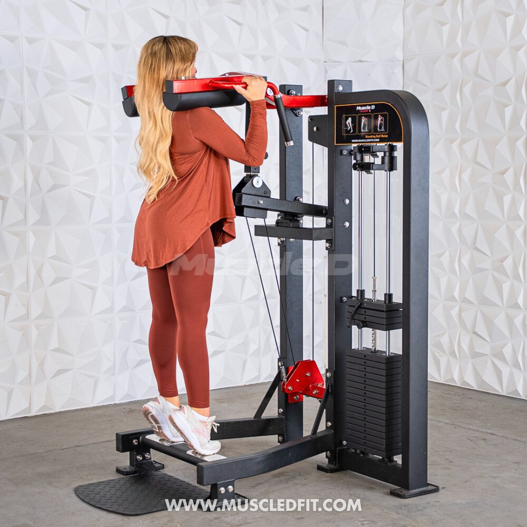 Woman using a Classic V2 Selectorized Standing Calf Raise machine in a gym setting with a textured white wall background.