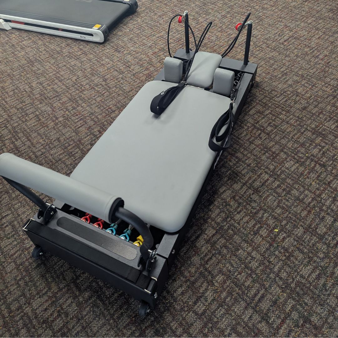 sleek light grey pilates reformer table with padded platform, adjustable foot bar, and sturdy metal frame for home or studio use